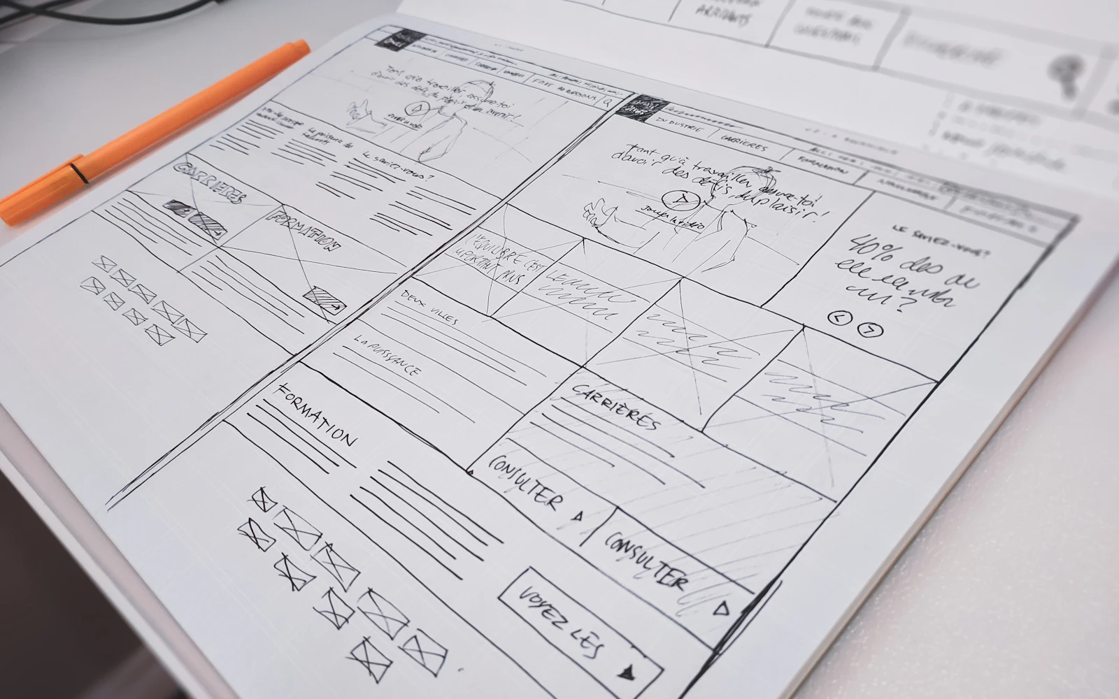 Hand-drawn website wireframes on paper beside an orange pen